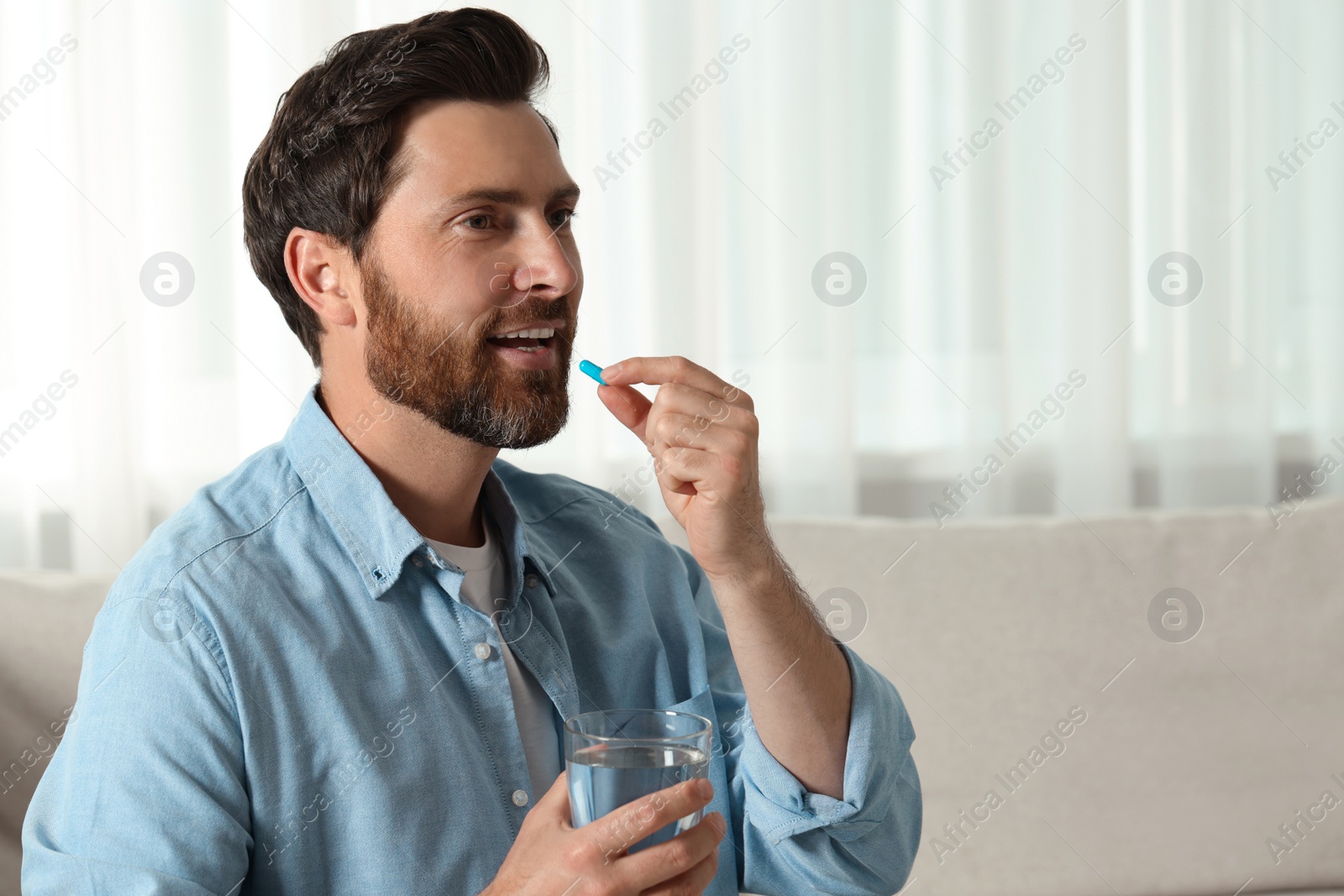 Photo of Handsome man with glass of water taking pill at home, space for text