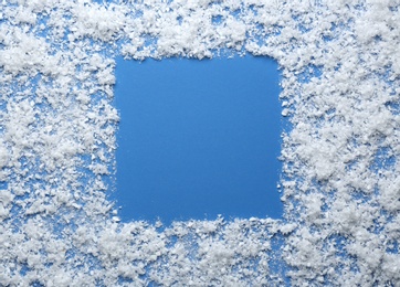 Frame made of snow on blue background, top view with space for text. Winter season