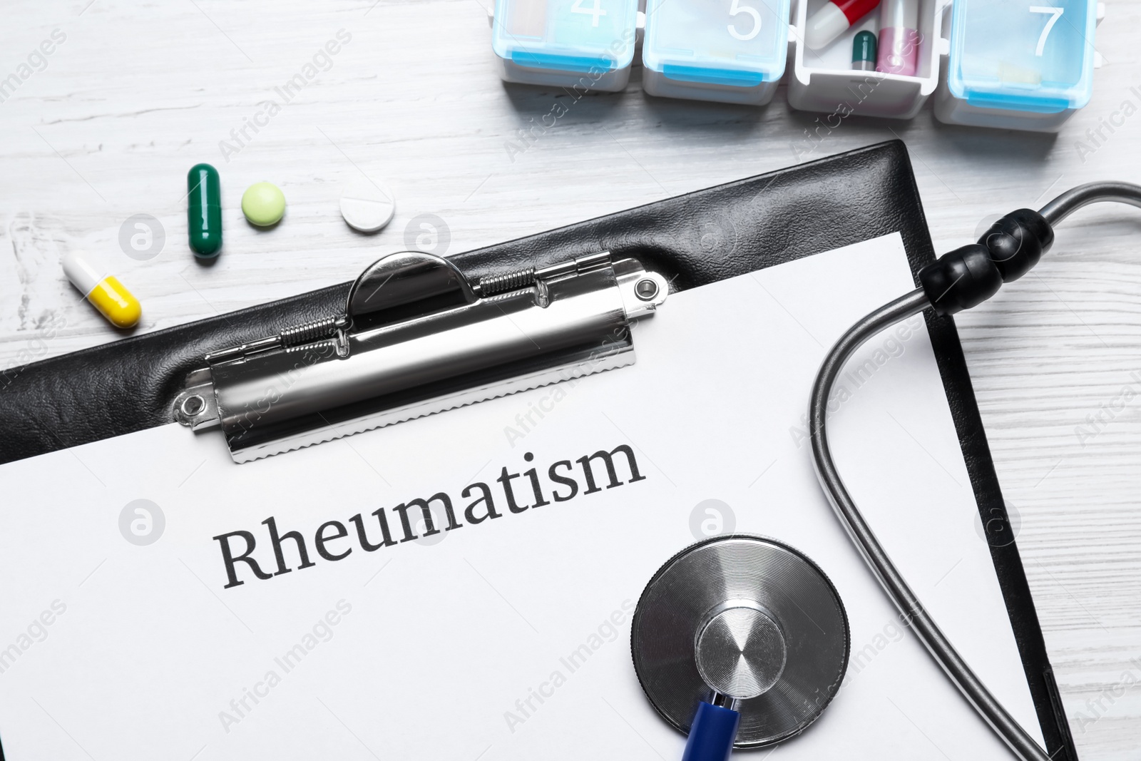 Photo of Clipboard with word Rheumatism, stethoscope and pills on white wooden table, flat lay