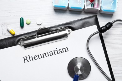 Photo of Clipboard with word Rheumatism, stethoscope and pills on white wooden table, flat lay
