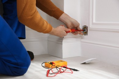 Photo of Electrician with screwdriver repairing power socket indoors, closeup