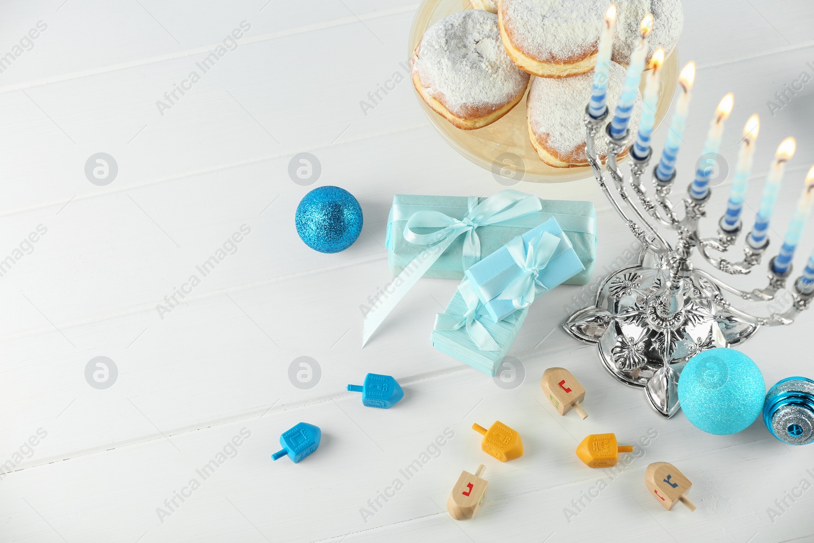 Photo of Composition with Hanukkah menorah, dreidels and gift boxes on white wooden table, above view. Space for text