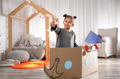 Cute little girl playing with cardboard boat in bedroom