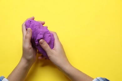 Photo of Woman playing with kinetic sand on yellow background, top view. Space for text