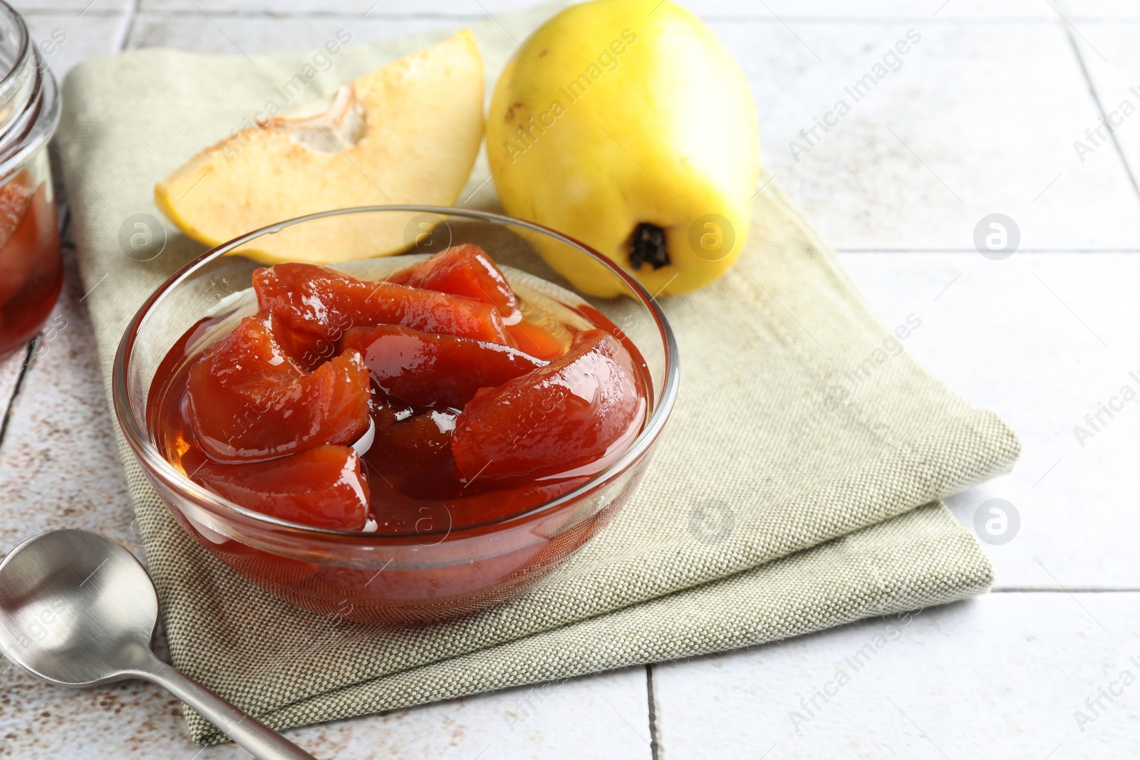 Photo of Tasty homemade quince jam in bowl and fruits on tiled table, closeup. Space for text