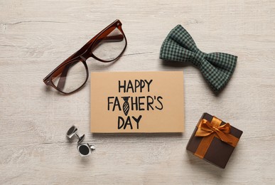 Photo of Card with phrase Happy Father's Day, gift box and different men accessories on wooden background, flat lay