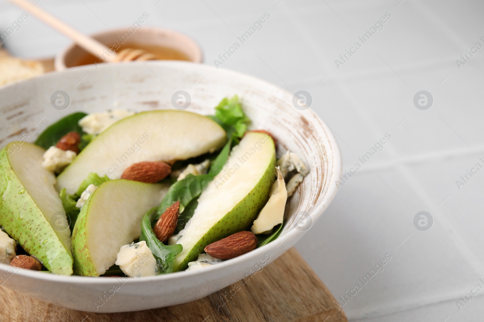 Photo of Delicious pear salad in bowl on light tiled table, closeup. Space for text