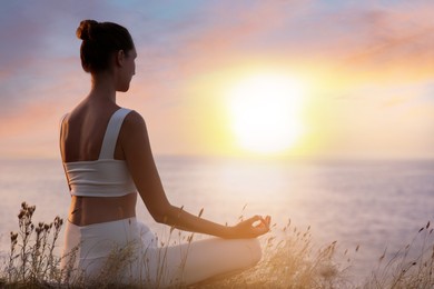 Image of Woman meditating near sea at sunset. Practicing yoga