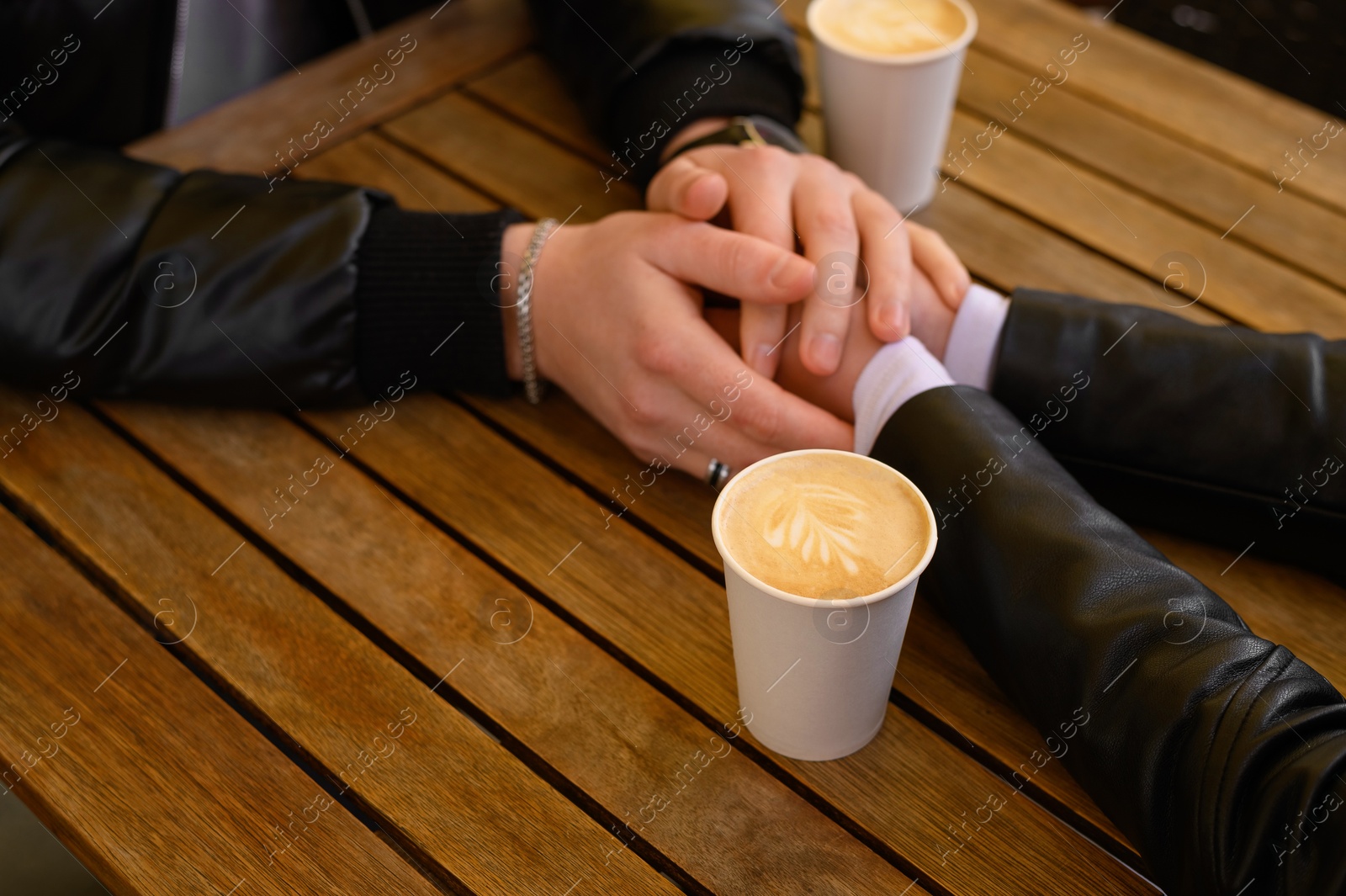 Photo of Lovely couple with coffee holding hands together at wooden table outdoors, closeup. Romantic date