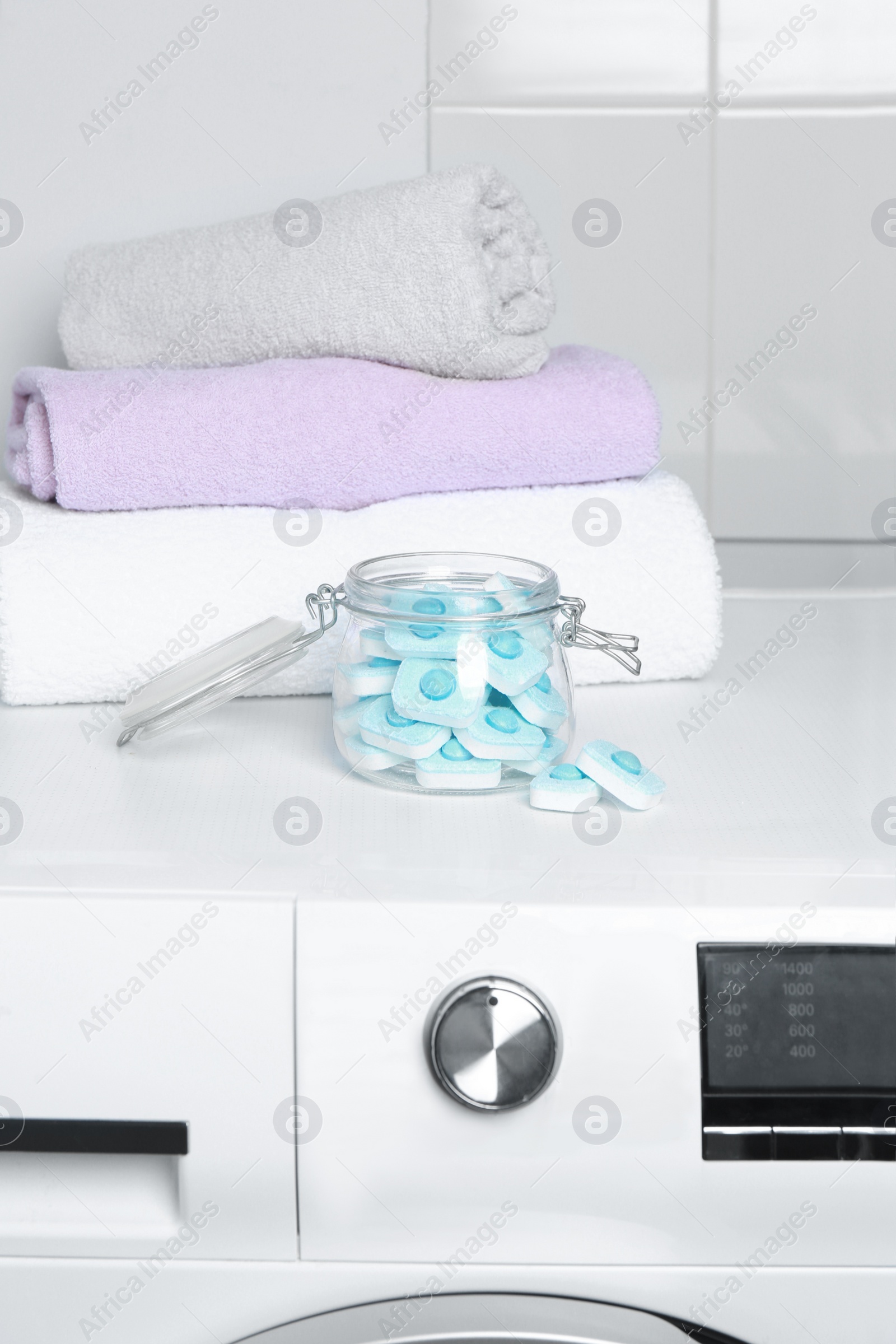 Photo of Jar with water softener tablets near stacked towels on washing machine
