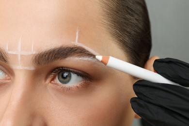 Beautician preparing young woman for procedure of permanent eyebrow makeup on grey background, closeup