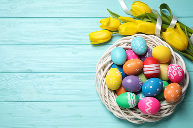 Photo of Colorful Easter eggs in decorative nest and tulip flowers on light blue wooden background, flat lay. Space for text