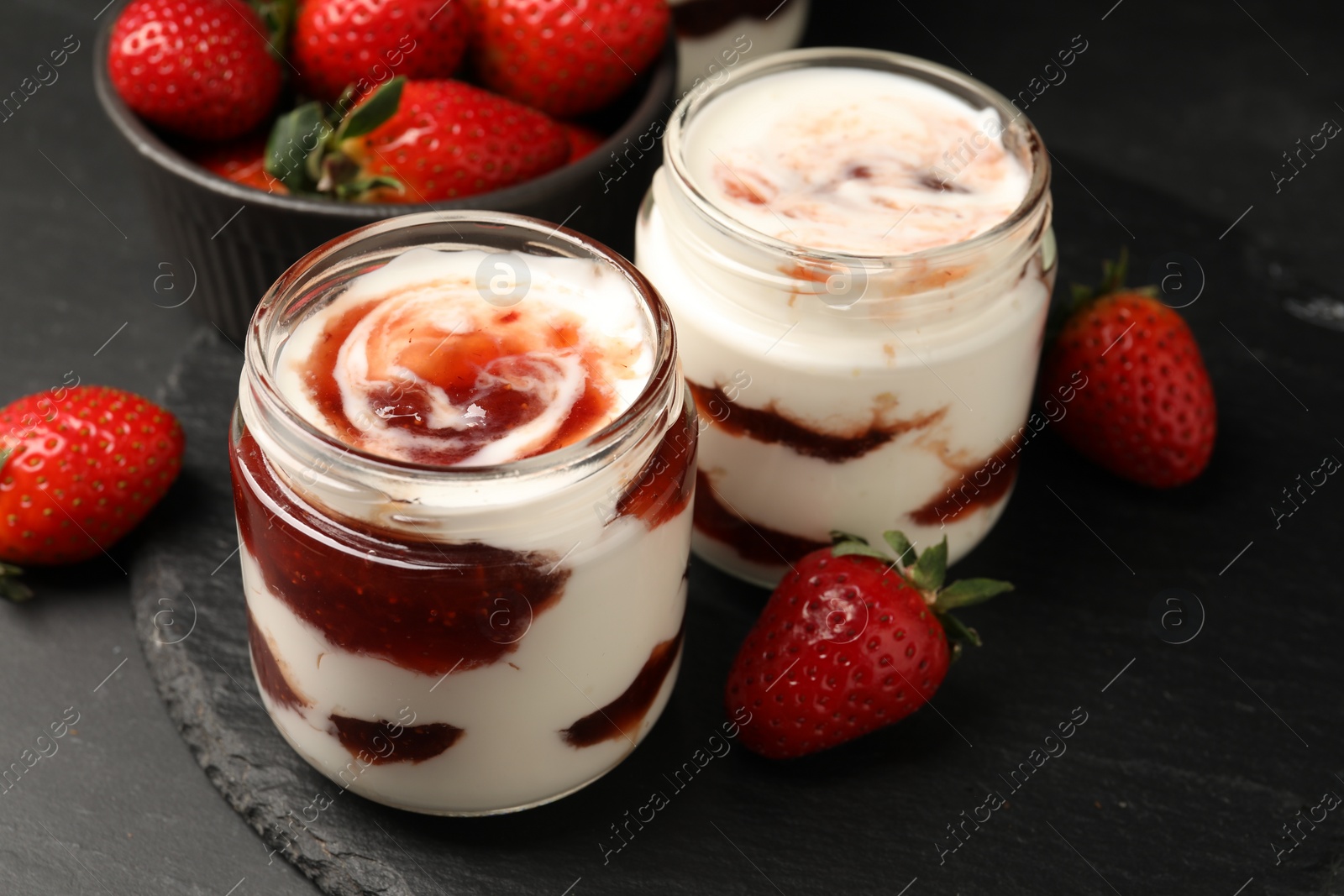 Photo of Tasty yoghurt with jam and strawberries on black table, closeup