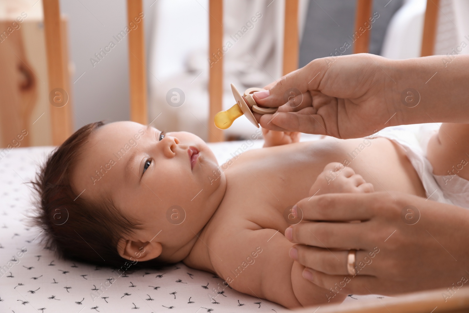 Photo of Mother giving pacifier to her cute little baby in crib at home, closeup