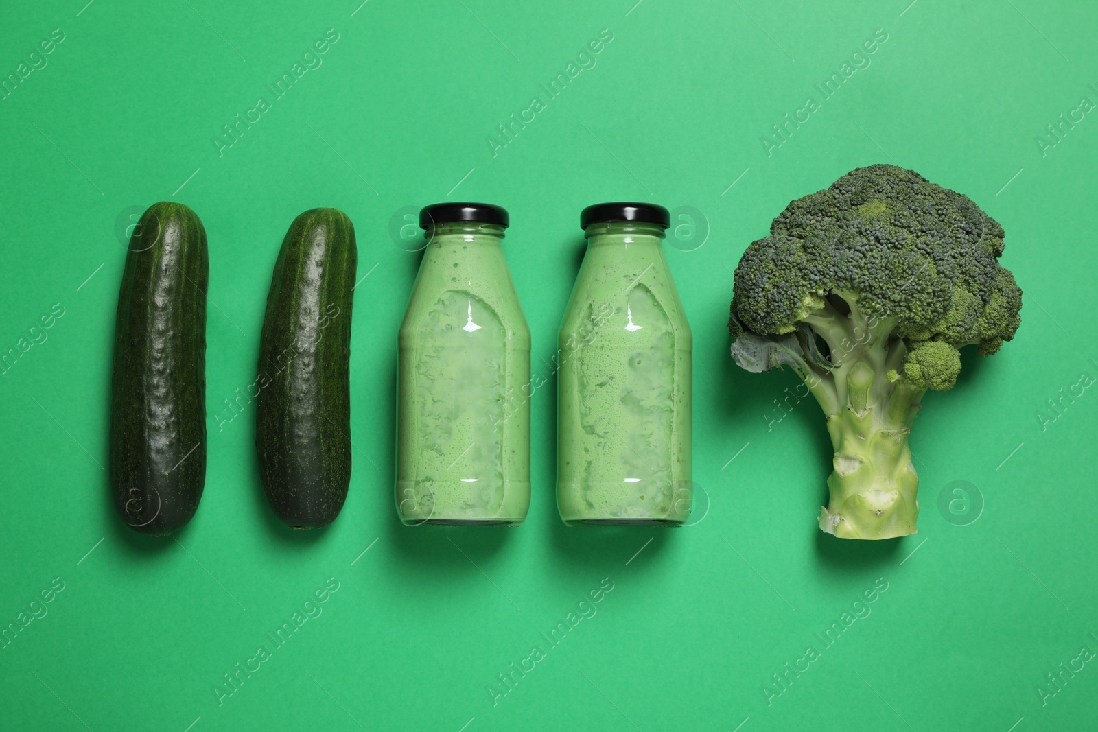 Photo of Bottles of delicious smoothie and ingredients on green background, flat lay