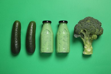 Bottles of delicious smoothie and ingredients on green background, flat lay