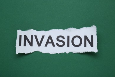 Photo of Piece of torn paper with word Invasion on green background, top view