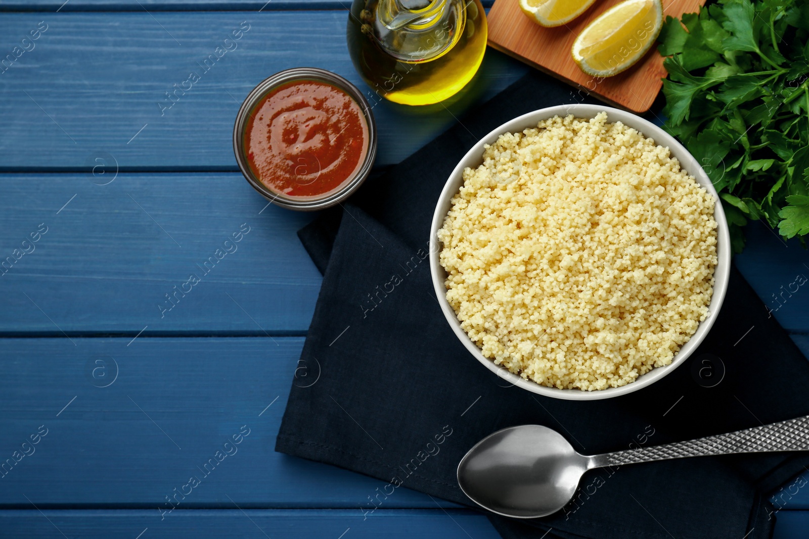 Photo of Tasty couscous and ingredients on blue wooden table, flat lay. Space for text