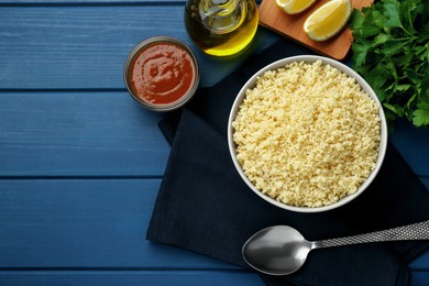 Photo of Tasty couscous and ingredients on blue wooden table, flat lay. Space for text