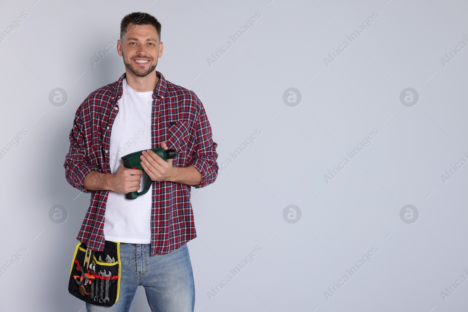 Photo of Handsome worker with electric drill on white background, space for text