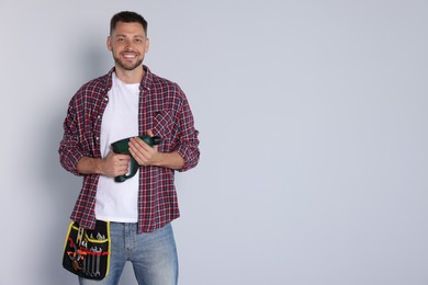Handsome worker with electric drill on white background, space for text