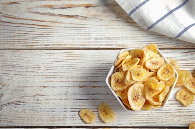 Bowl with sweet banana slices on wooden  table, top view with space for text. Dried fruit as healthy snack