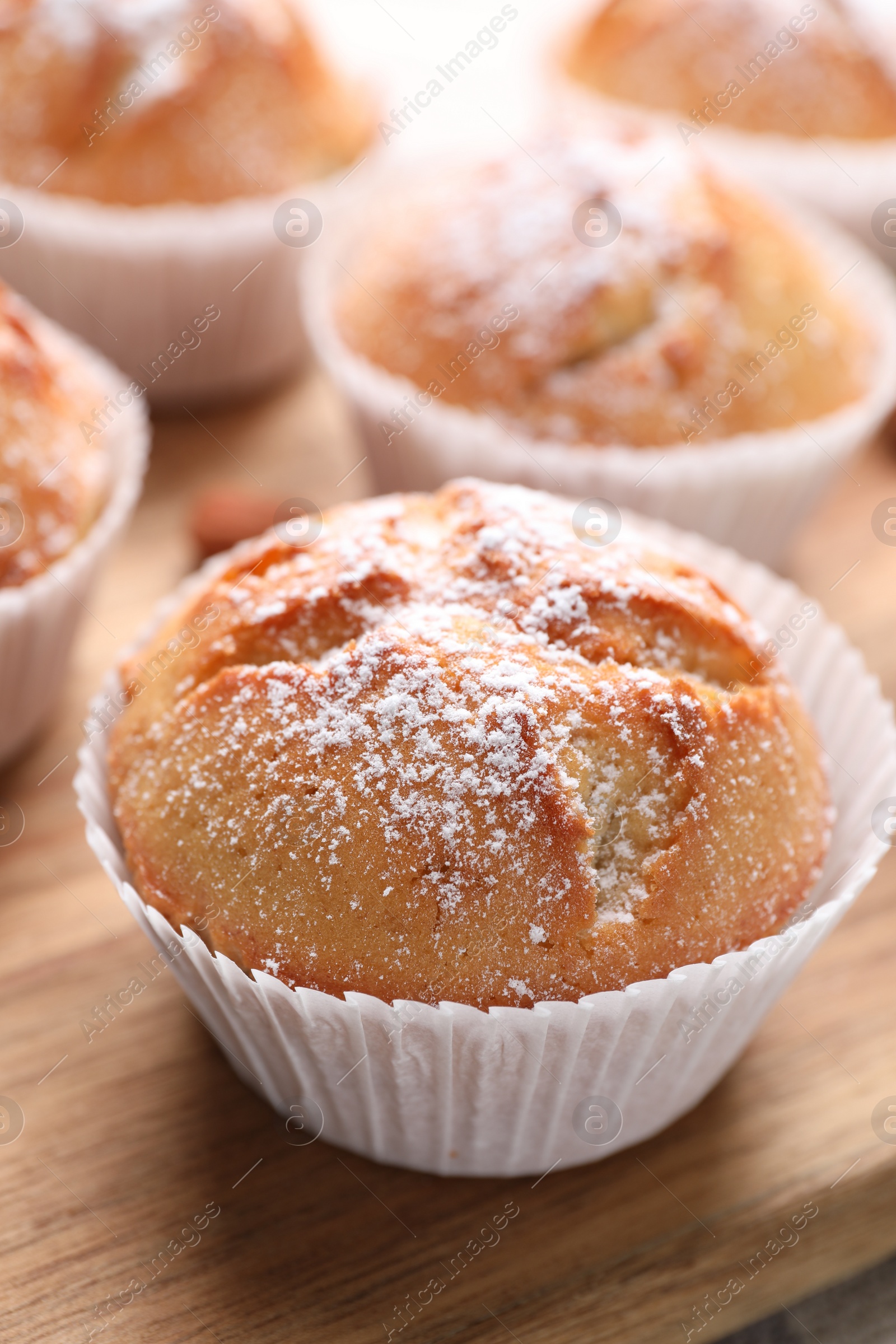 Photo of Tasty muffins powdered with sugar on wooden board, closeup