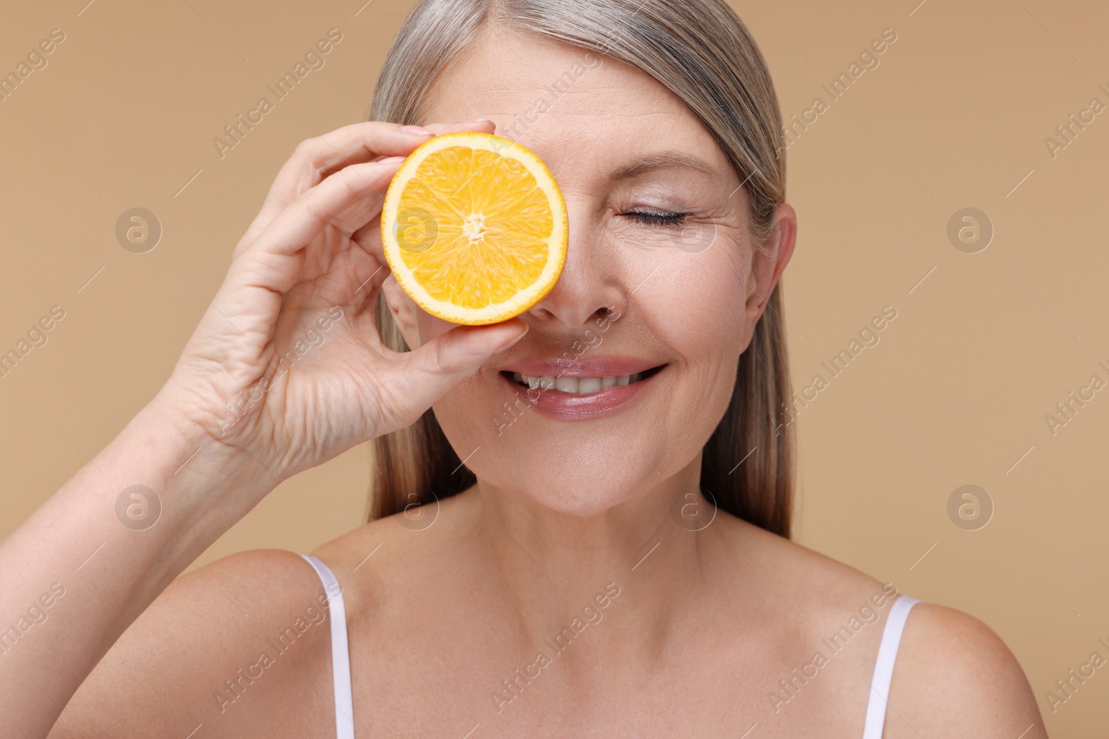 Photo of Beautiful woman with half of orange rich in vitamin C on beige background