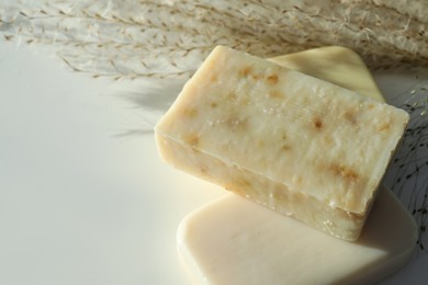 Photo of Different soap bars and dried plant on white table, closeup. Space for text