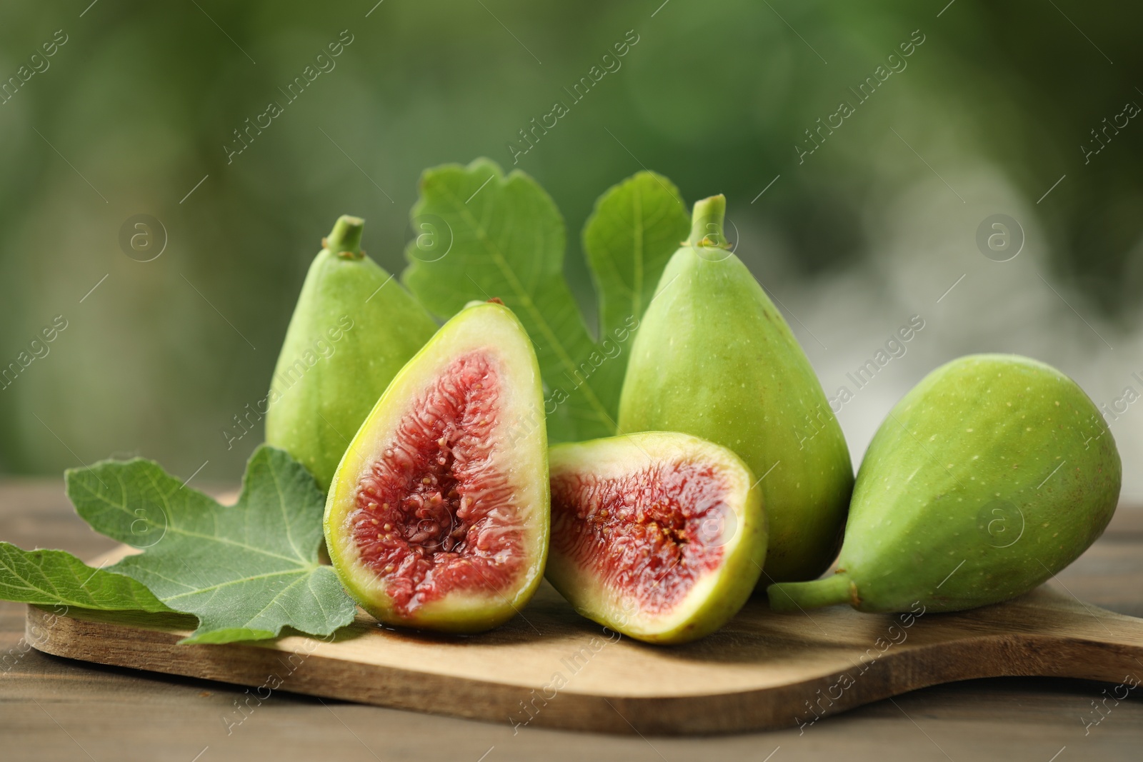 Photo of Cut and whole green figs on table against blurred background, closeup