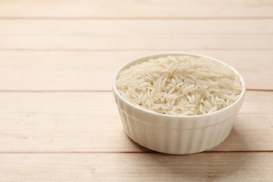 Photo of Raw basmati rice in bowl on white wooden table, closeup. Space for text
