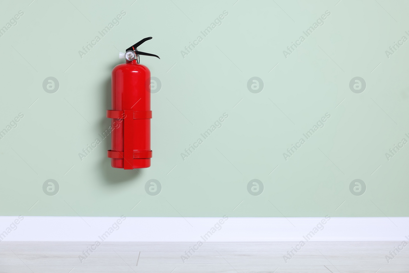 Photo of Red fire extinguisher on light green wall. Space for text