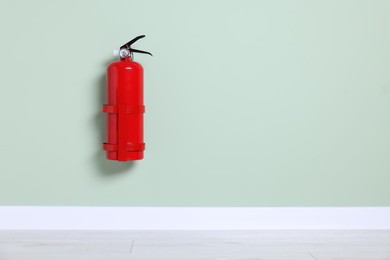 Red fire extinguisher on light green wall. Space for text