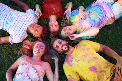 Photo of Happy friends covered with colorful powder dyes on green grass outdoors, above view. Holi festival celebration