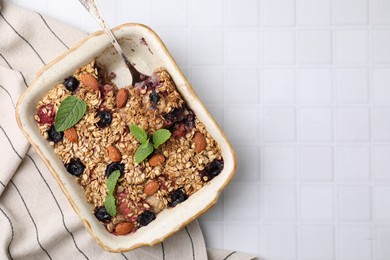 Photo of Tasty baked oatmeal with berries and almonds in baking tray on white tiled table, top view. Space for text
