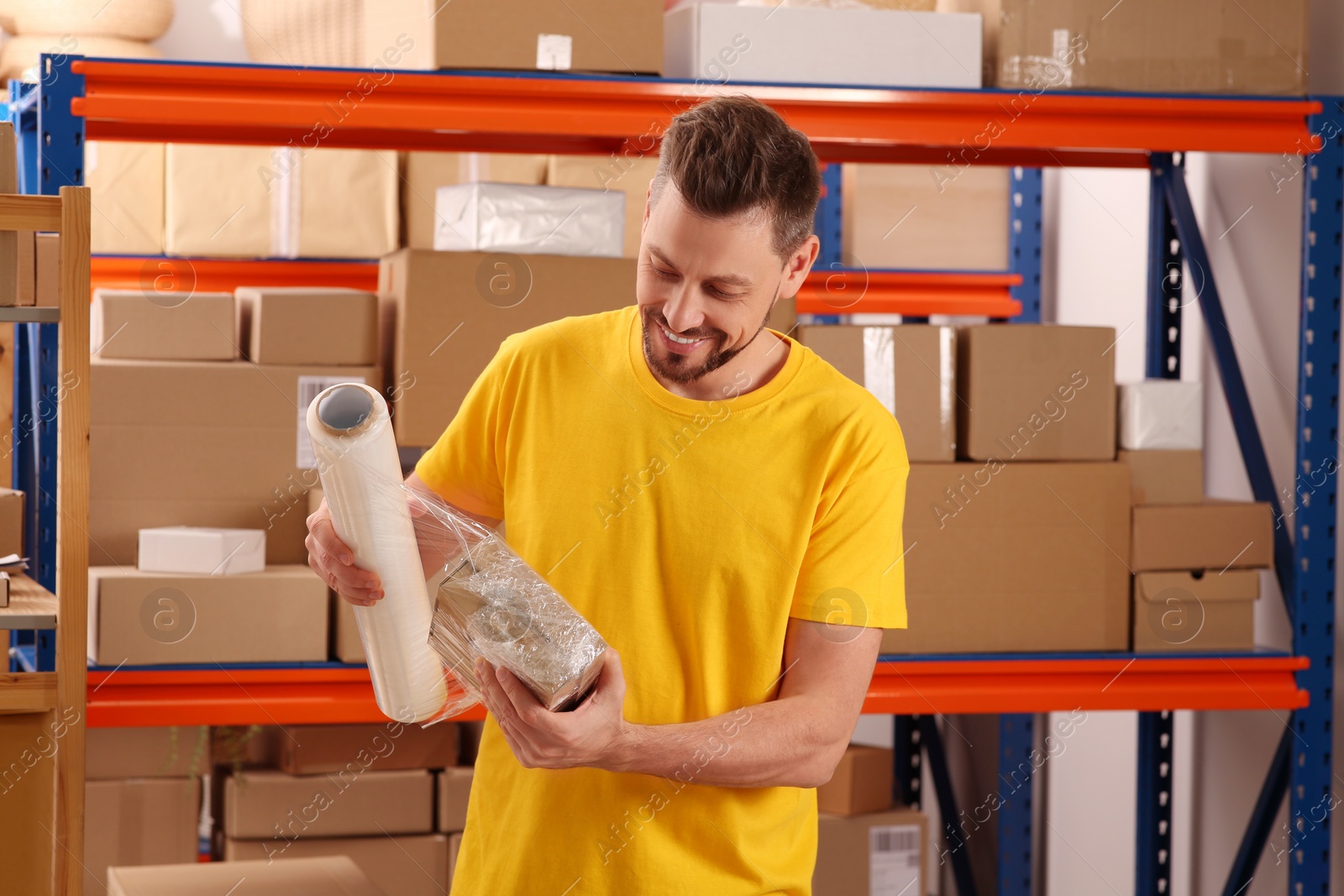 Photo of Post office worker wrapping parcel in stretch film indoors