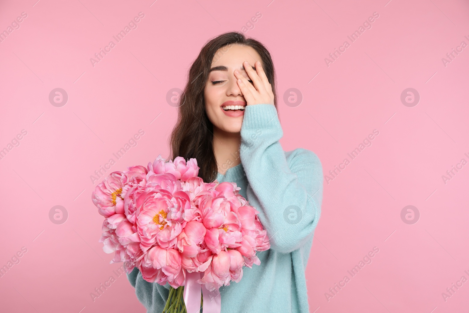 Photo of Beautiful young woman with bouquet of peonies on pink background