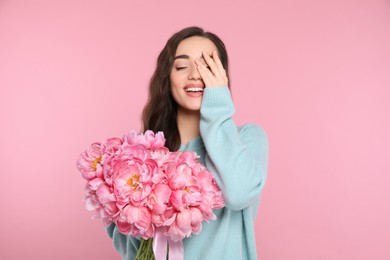 Beautiful young woman with bouquet of peonies on pink background