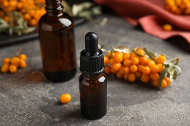 Ripe sea buckthorn and bottles of essential oil on grey table