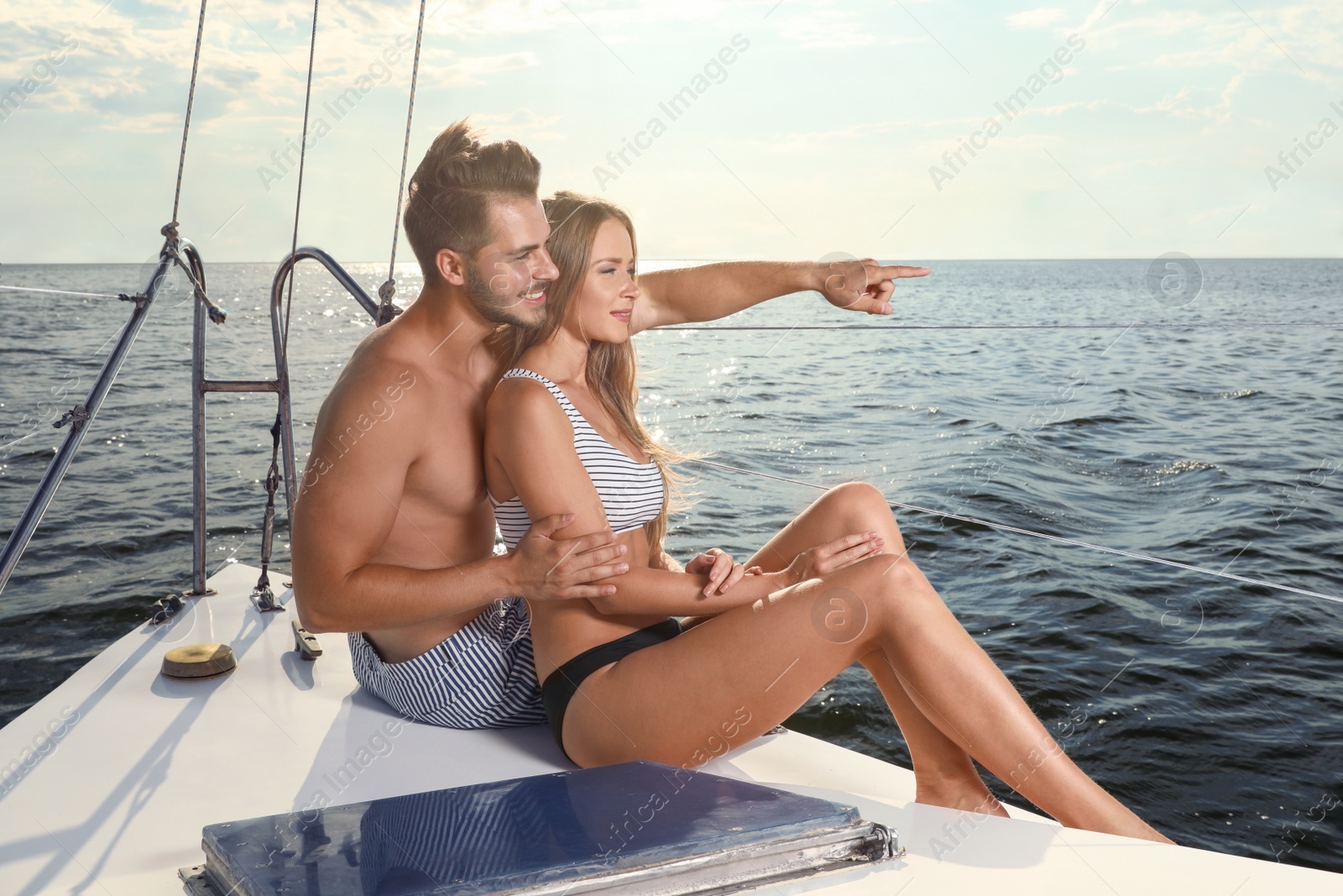 Photo of Young man and his beautiful girlfriend in bikini sitting on yacht. Happy couple on vacation