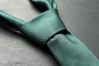 Photo of One green necktie on grey textured table, closeup