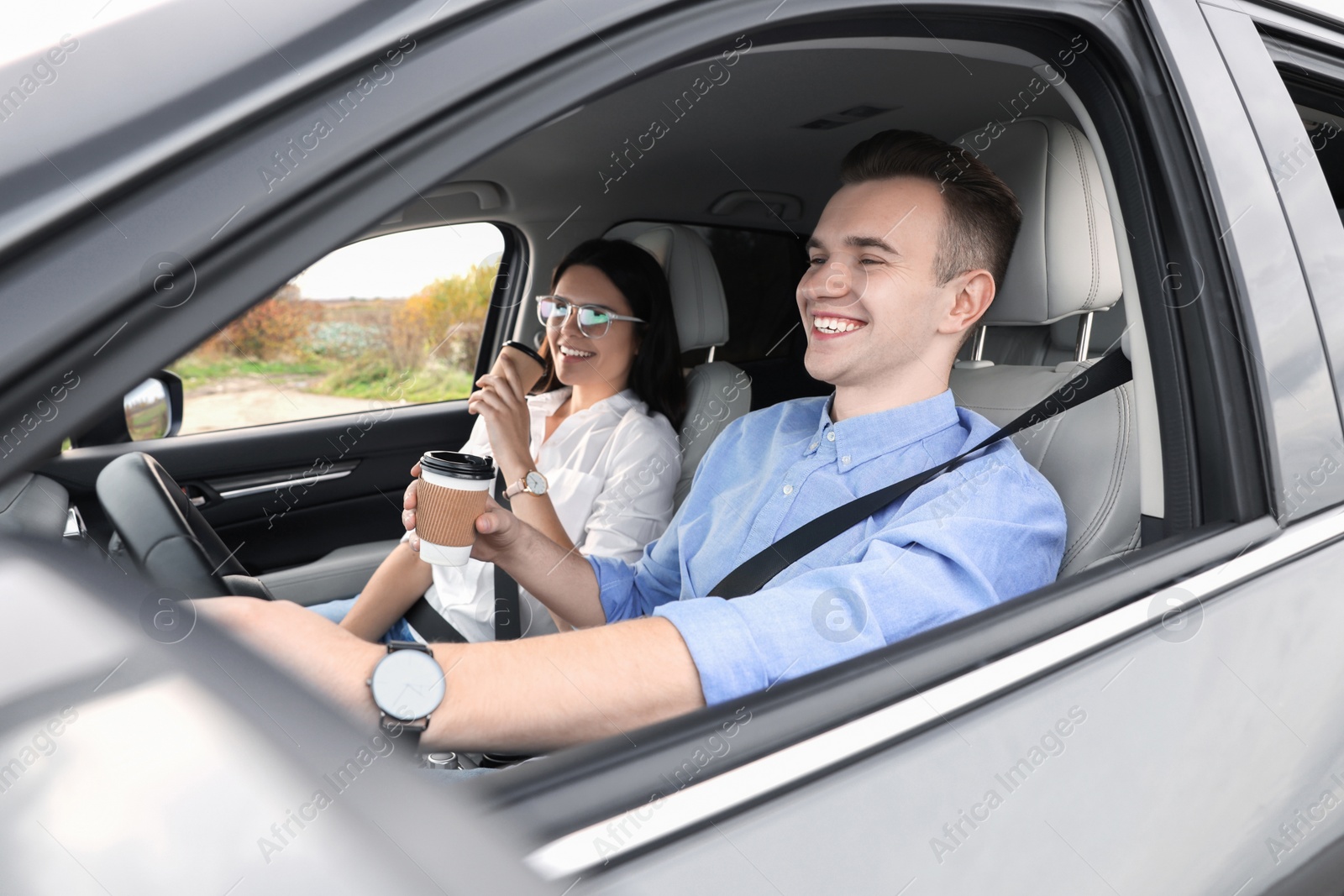Photo of Happy young couple with cups of coffee in car