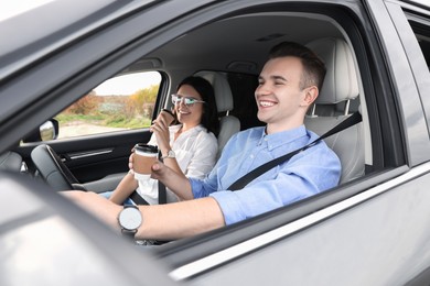 Happy young couple with cups of coffee in car