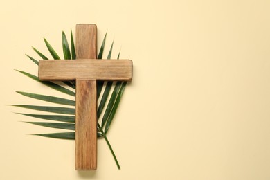 Photo of Wooden cross and palm leaf on beige background, top view with space for text. Easter attributes