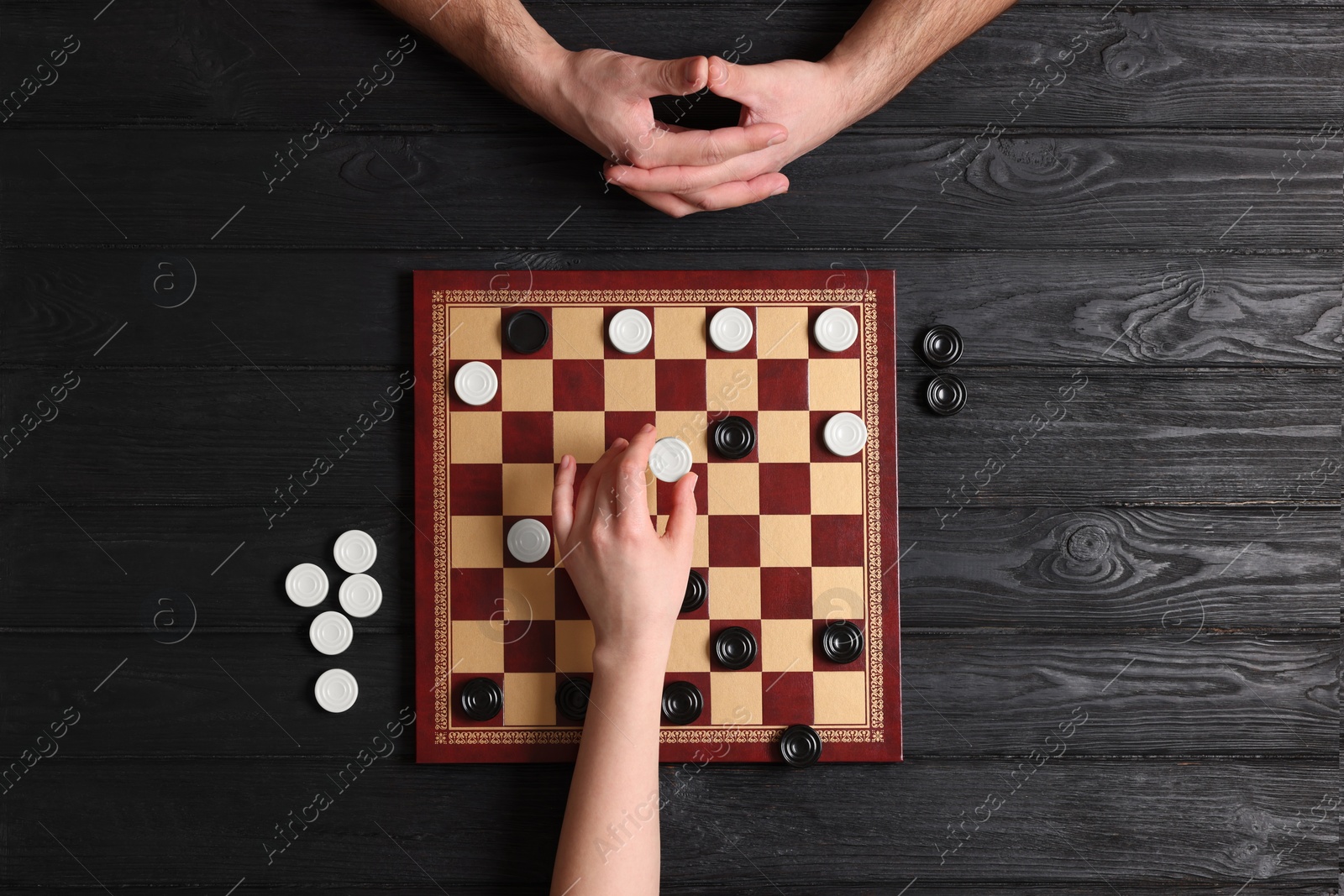 Photo of Man playing checkers with woman at black wooden table, top view