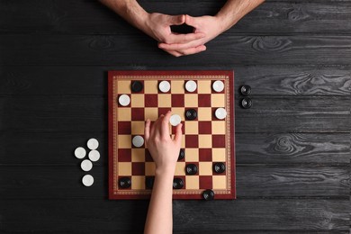 Photo of Man playing checkers with woman at black wooden table, top view