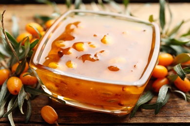 Delicious sea buckthorn jam and fresh berries on wooden table, closeup