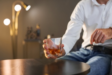 Man with glass of whiskey sitting at table, closeup. Space for text