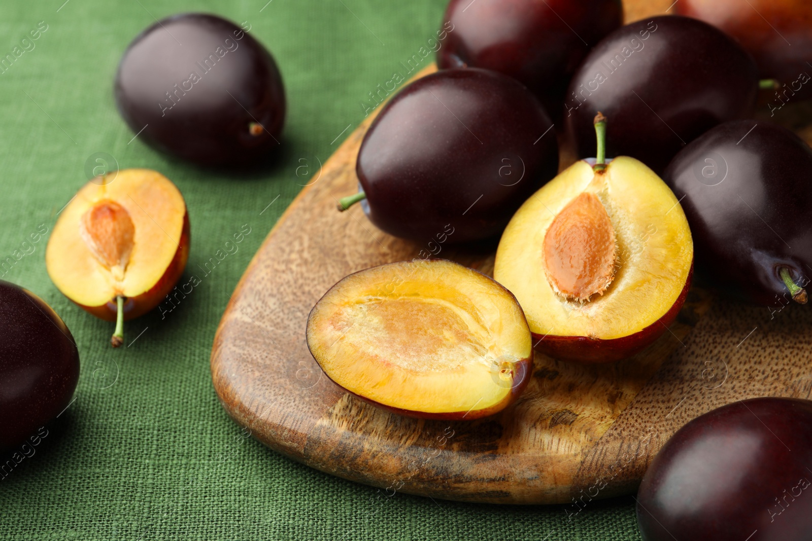 Photo of Many tasty ripe plums and wooden board on green fabric, closeup