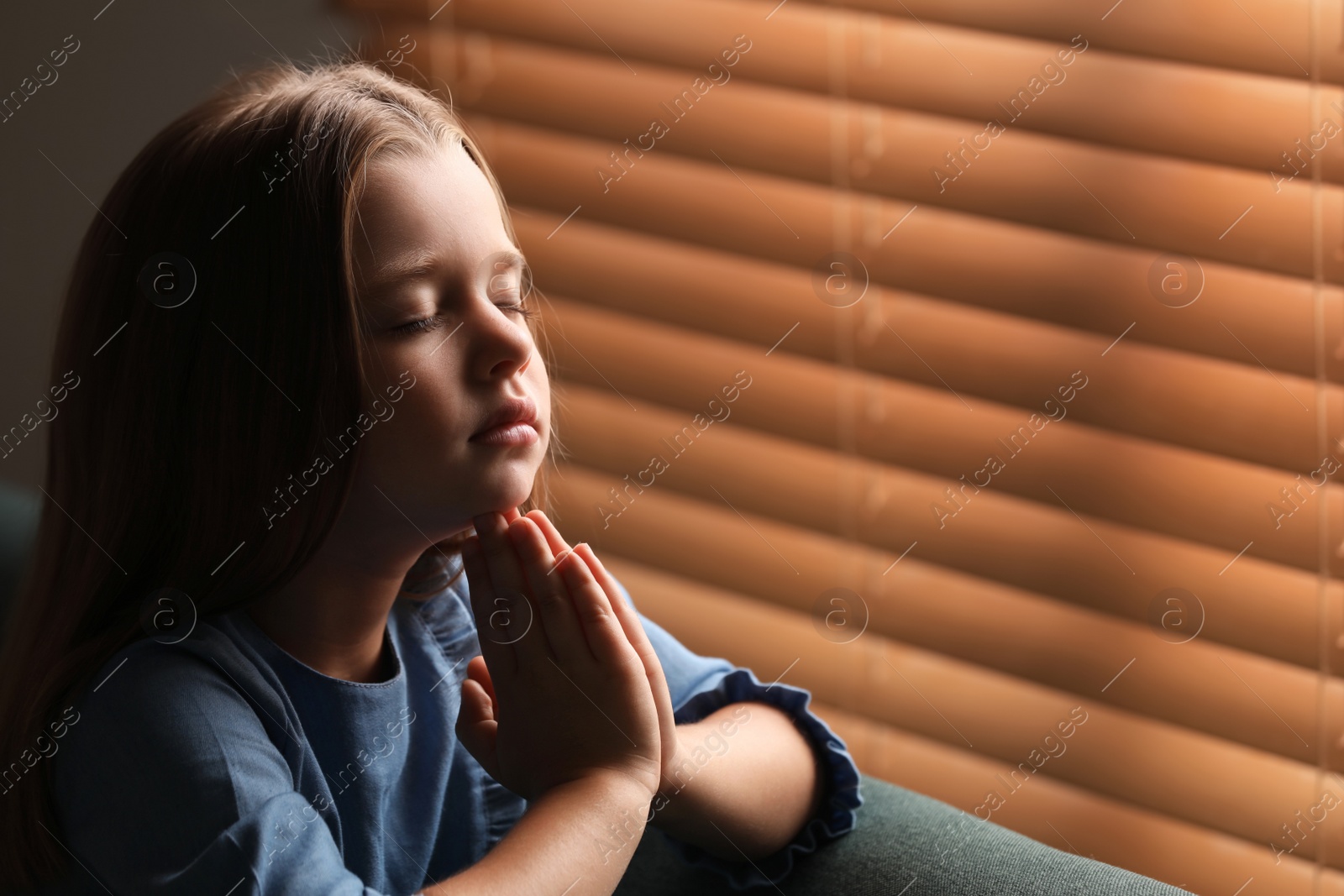 Photo of Cute little girl praying near window. Space for text